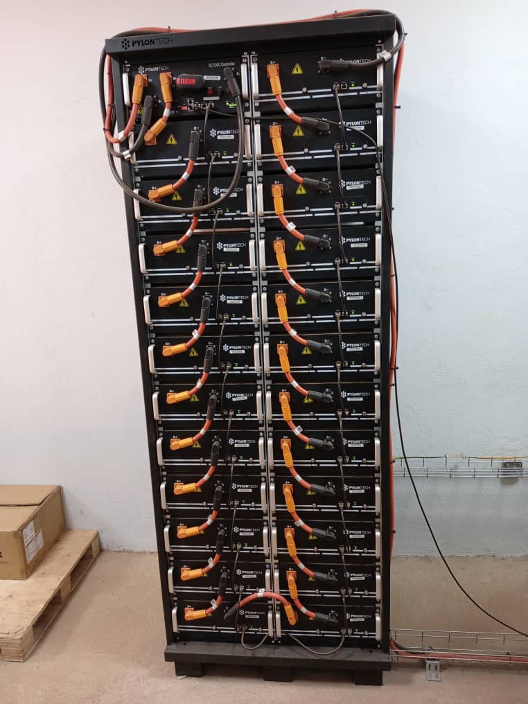 Rack de batteries lithium empilées en armoire, connecteurs de puissance orange et noirs raccordés module par module